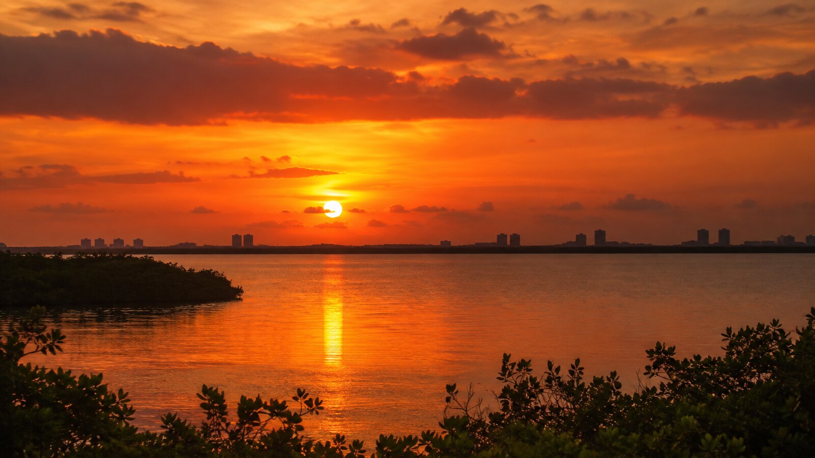 El sol descendiendo sobre la Laguna Nichupté, filtrado por la humedad tropical que satura los rojos y ámbares
